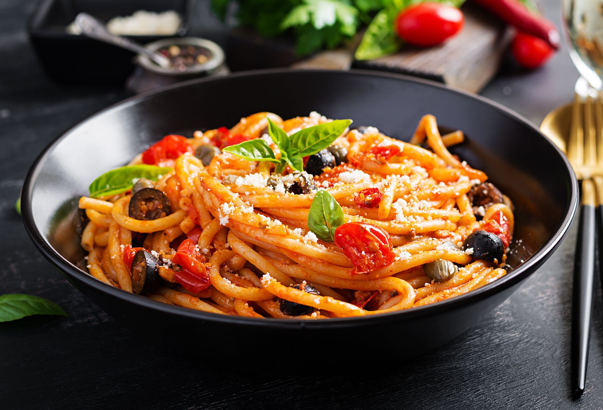 Eine Schüssel Spaghetti mit Tomatensoße und Oliven auf einem Tisch.