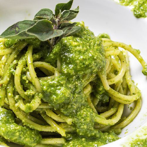 Eine Nahaufnahme einer Schüssel Spaghetti mit grüner Soße obendrauf.