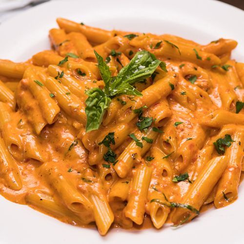 Eine Nahaufnahme eines Tellers Pasta mit Soße und Basilikum auf einem Tisch.
