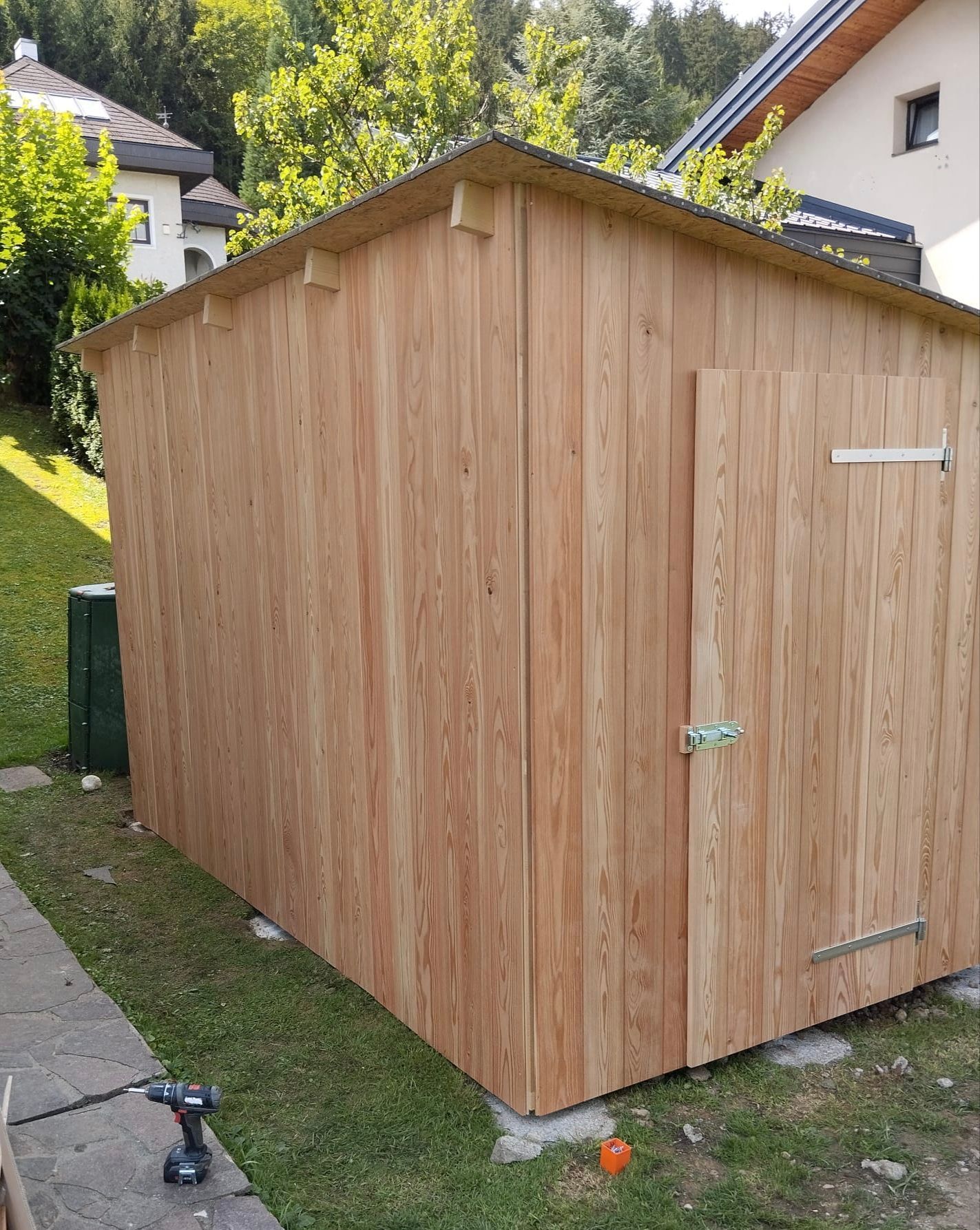 Vor einem Haus steht im Gras ein Holzschuppen.