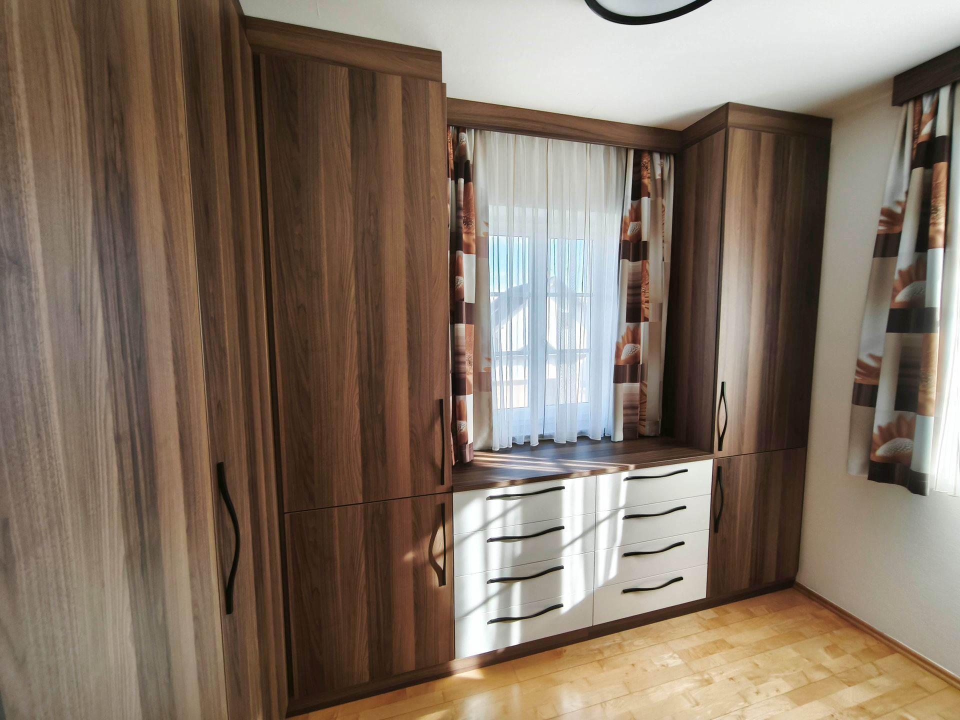 Ein Schlafzimmer mit Holzschränken und einem Fenster mit Vorhängen.
