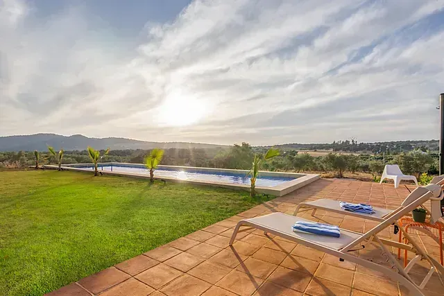 Un patio con sillas de jardín y una piscina al fondo.