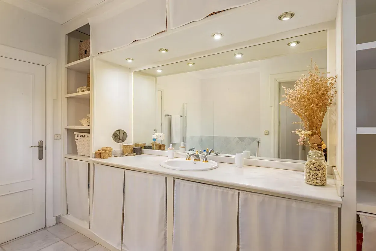 Un baño con un gran espejo, lavabo y armarios.