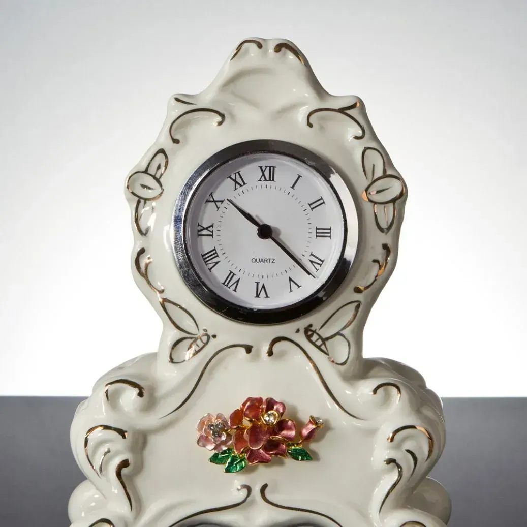 Un reloj blanco con números romanos y una flor.