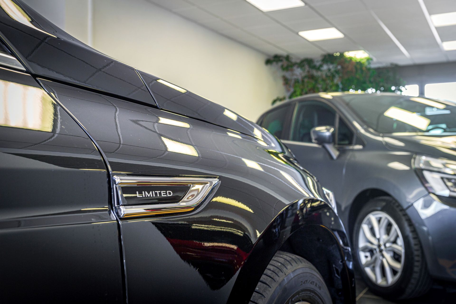 Gros plan sur le panneau latéral d'une voiture noire arborant un badge LIMITED, avec une voiture floue en arrière-plan dans une salle d'exposition.