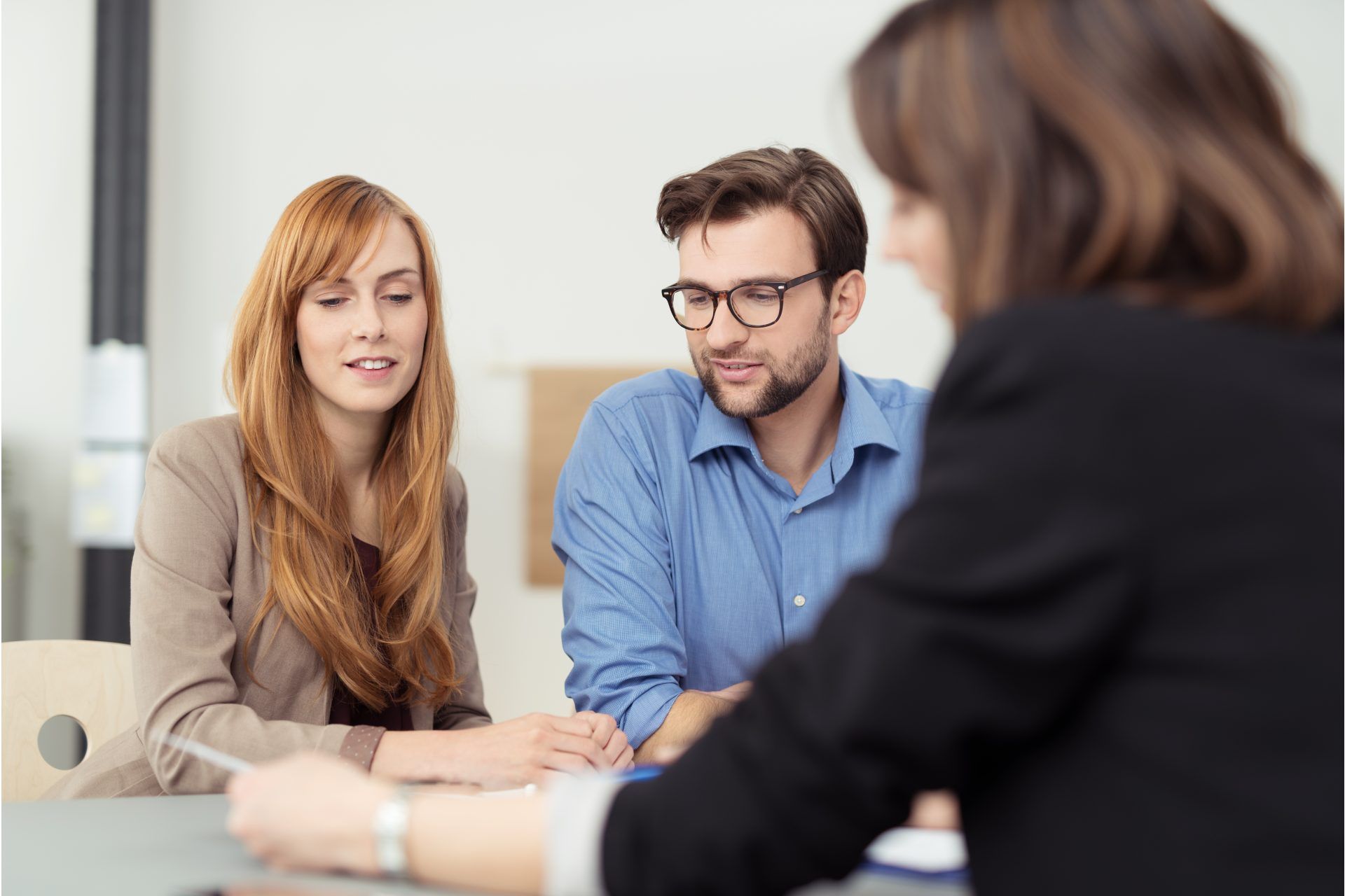 Trois personnes sont assises autour d'une table dans un cadre professionnel, concentrées sur un document lors d'une réunion.