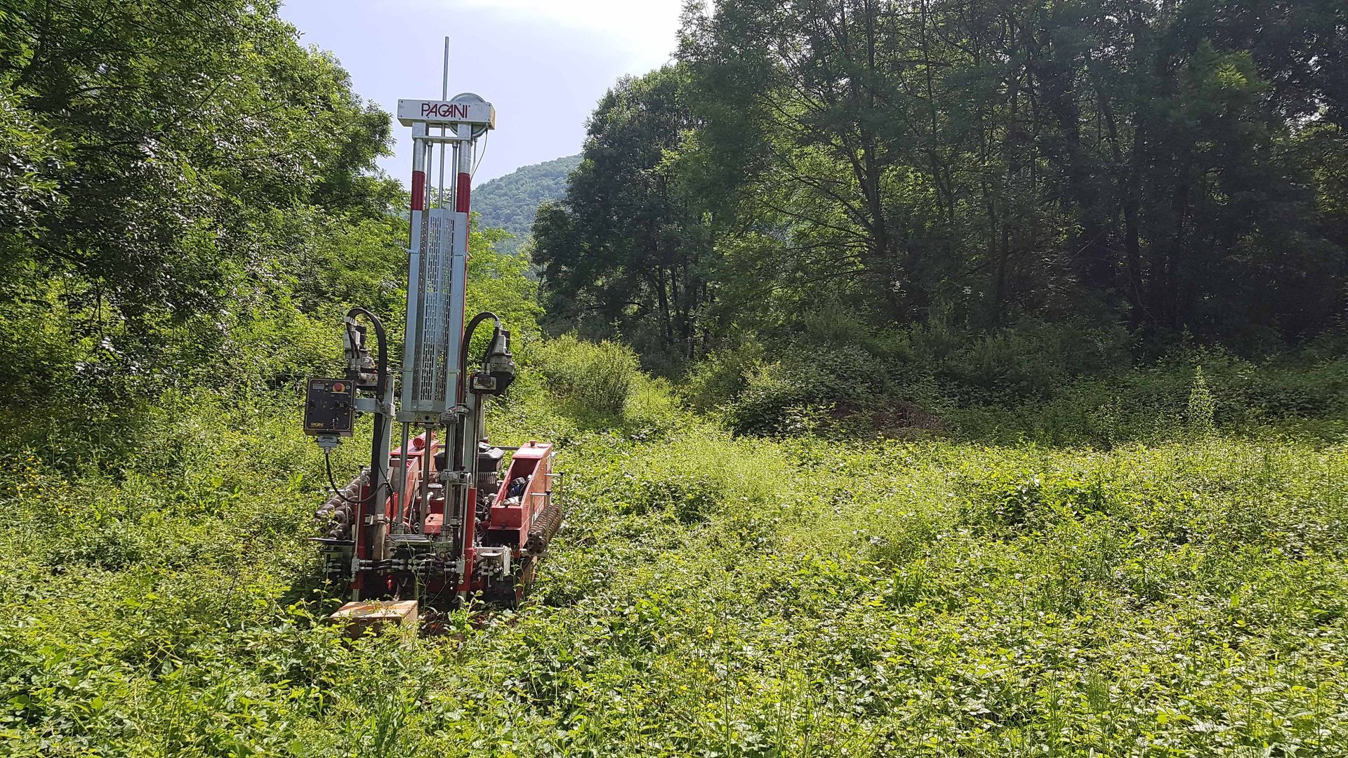 Par une belle journée, une foreuse compacte se dresse au milieu d'un champ dense et verdoyant, entouré d'arbres.