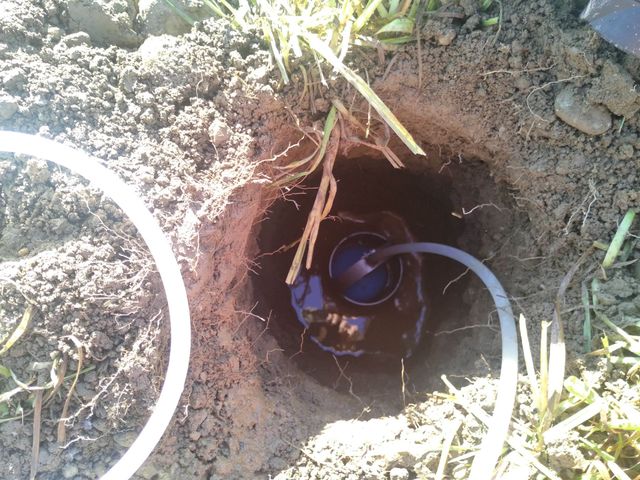 Une pompe submersible bleue est installée dans un trou étroit creusé dans le sol, avec un câble d'alimentation qui en sort.