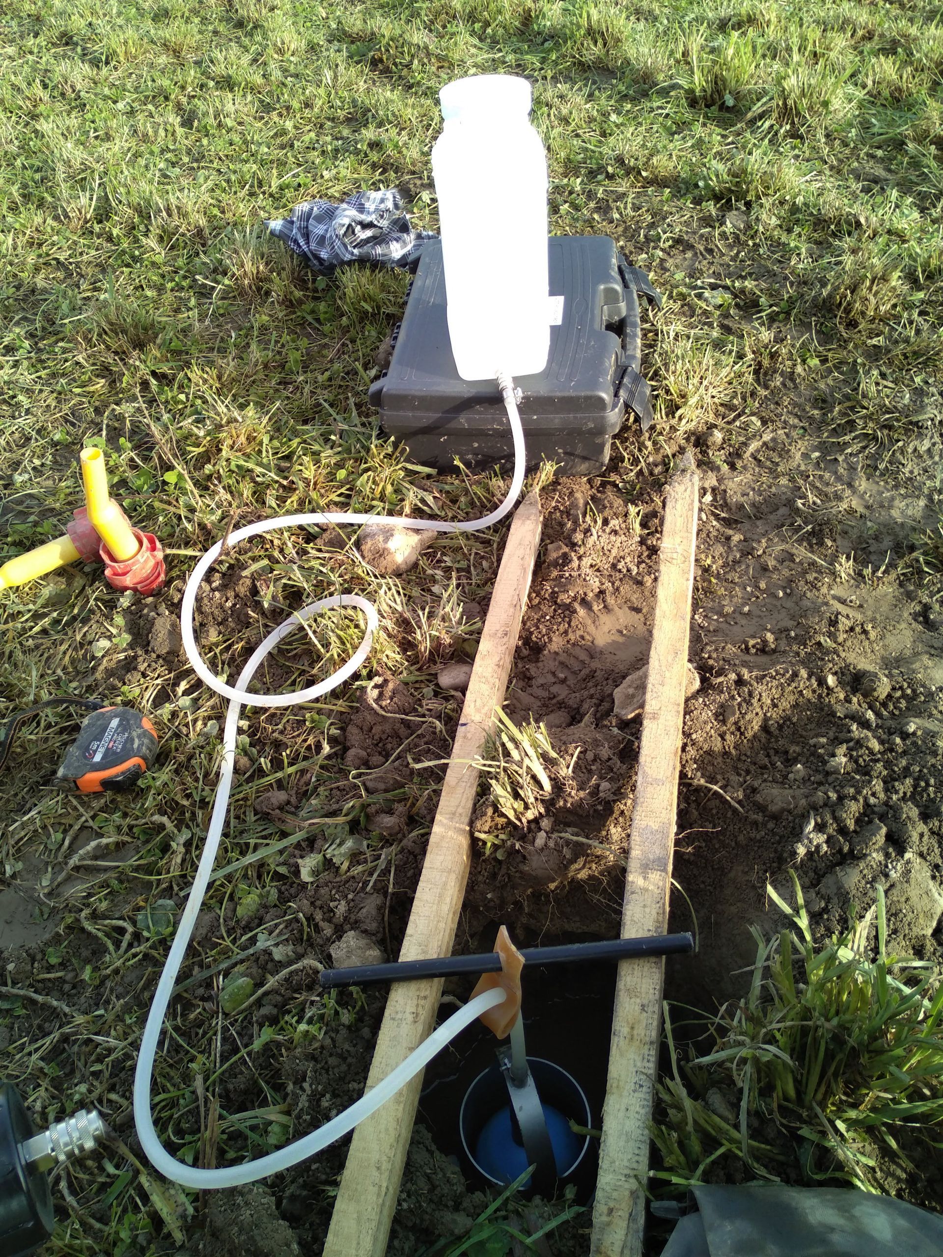 Une main tient un appareil électronique portatif à côté d'un enrouleur de câble jaune posé sur une surface gravillonnée.