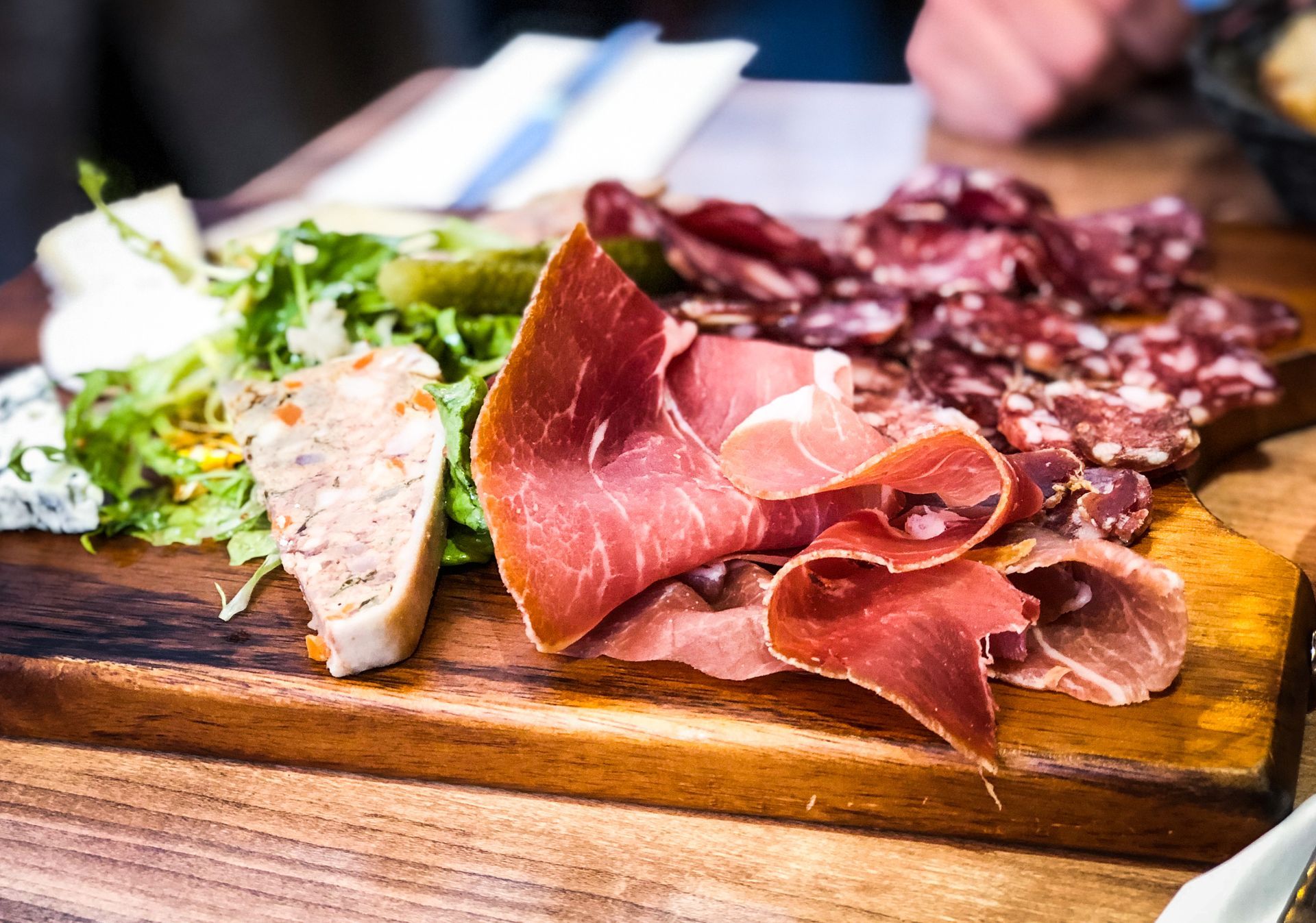 Planche de charcuterie avec jambon, saucisson, terrine et salade verte sur un plateau en bois.