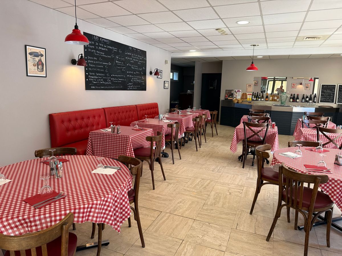 Café vide avec des tables à damier rouge et blanc, des banquettes rouges et un comptoir au fond.