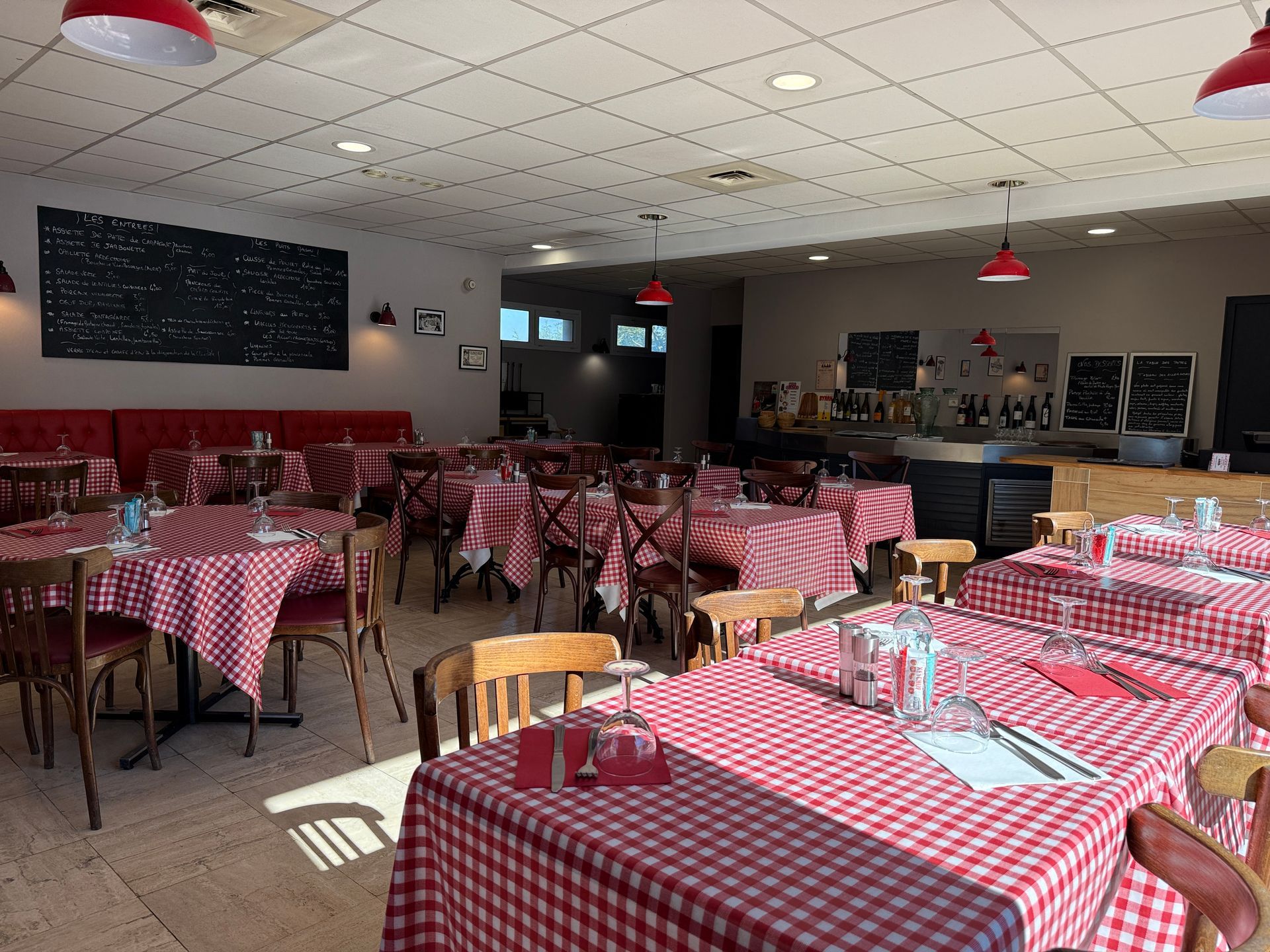 Restaurant, nappes à carreaux rouges et chaises en bois, éclairé par la lumière du soleil et des lampes rouges suspendues.