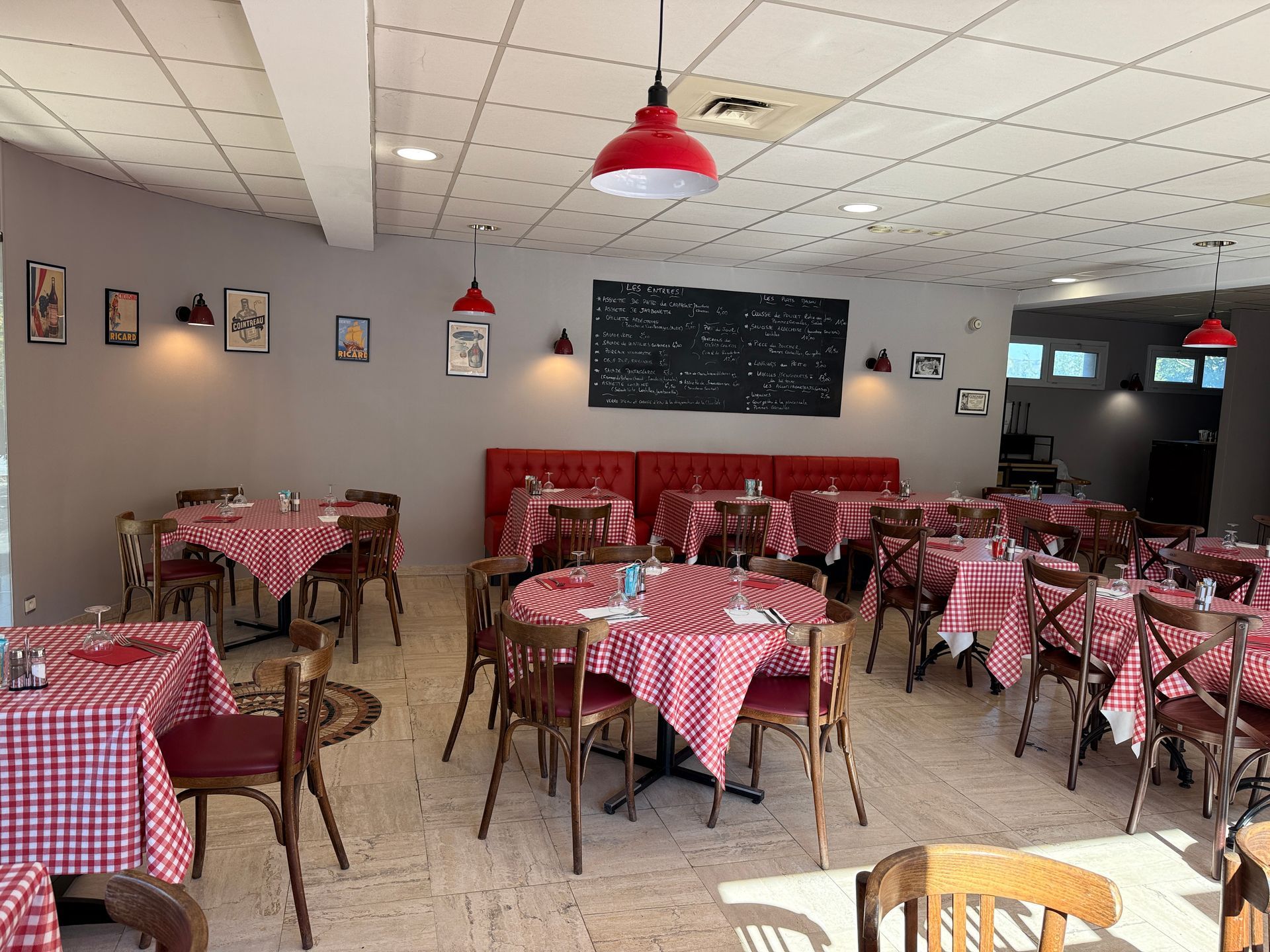 Salle à manger de restaurant vide avec tables à carreaux rouges, chaises en bois et suspensions lumineuses rouges.