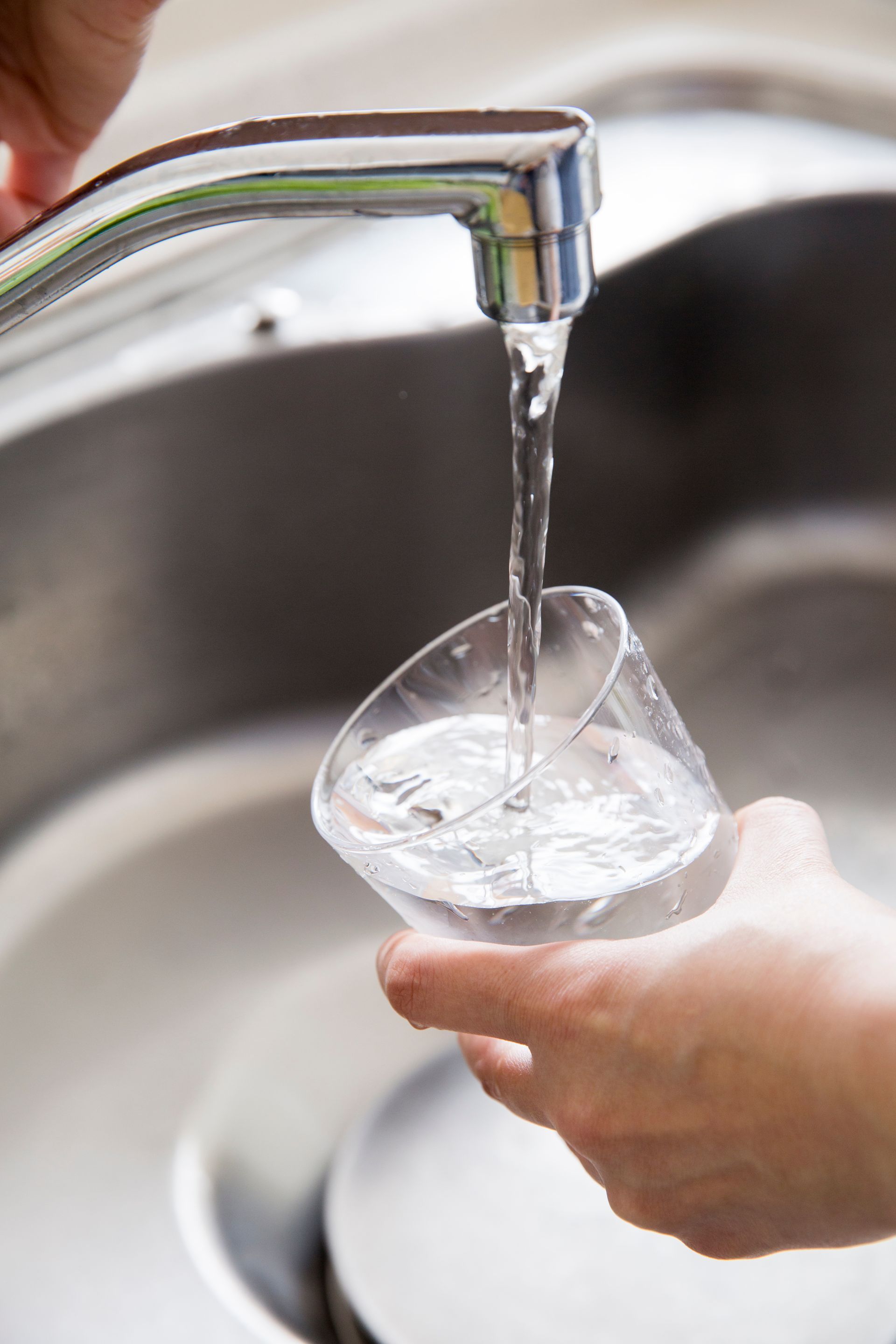 Personne remplissant un verre avec de l'eau provenant d'un robinet chromé dans un évier en acier inoxydable.