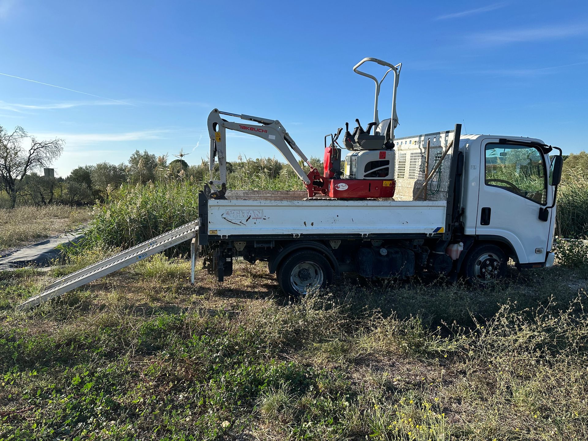 Camion blanc avec une minipelle dans la benne.