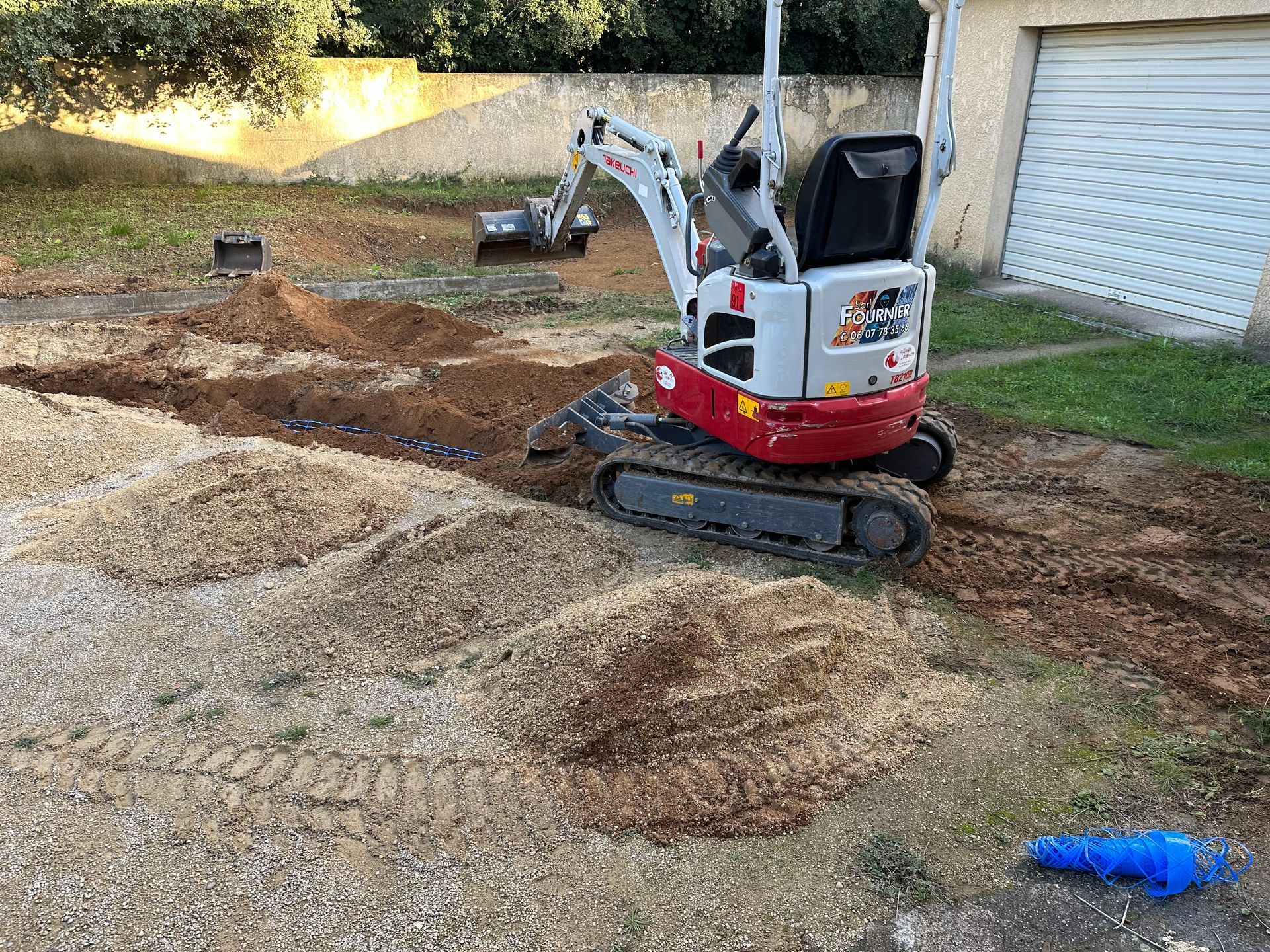 Camion blanc avec une minipelle dans la benne, rampe étendue sur un terrain herbeux sous un ciel bleu.