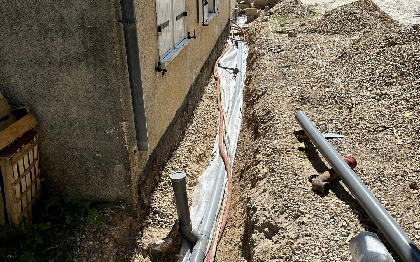 Une tranchée à côté d'un bâtiment avec des tuyaux, doublée de matériaux de protection.