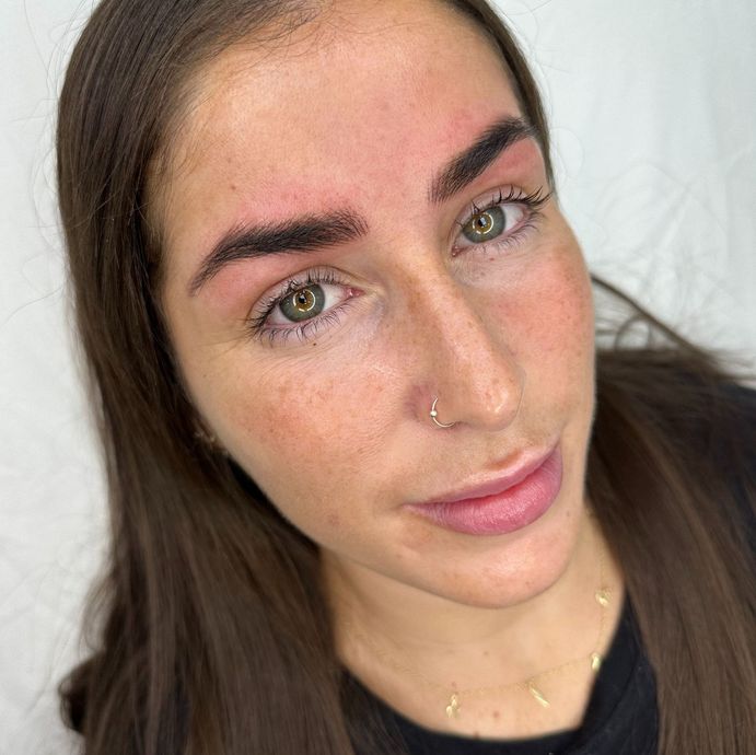 Mujer con cejas recién tatuadas, piel rosada y un piercing en la nariz.