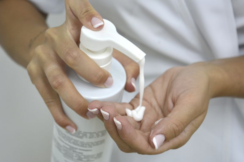 Persona vertiendo loción de una botella blanca en su mano.
