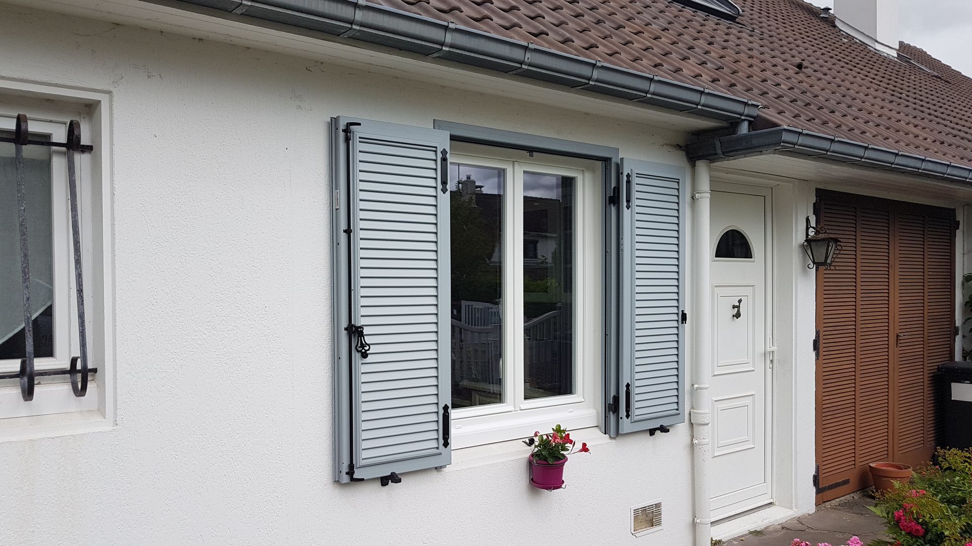 Une fenêtres avec des volets gris et un pot de fleurs