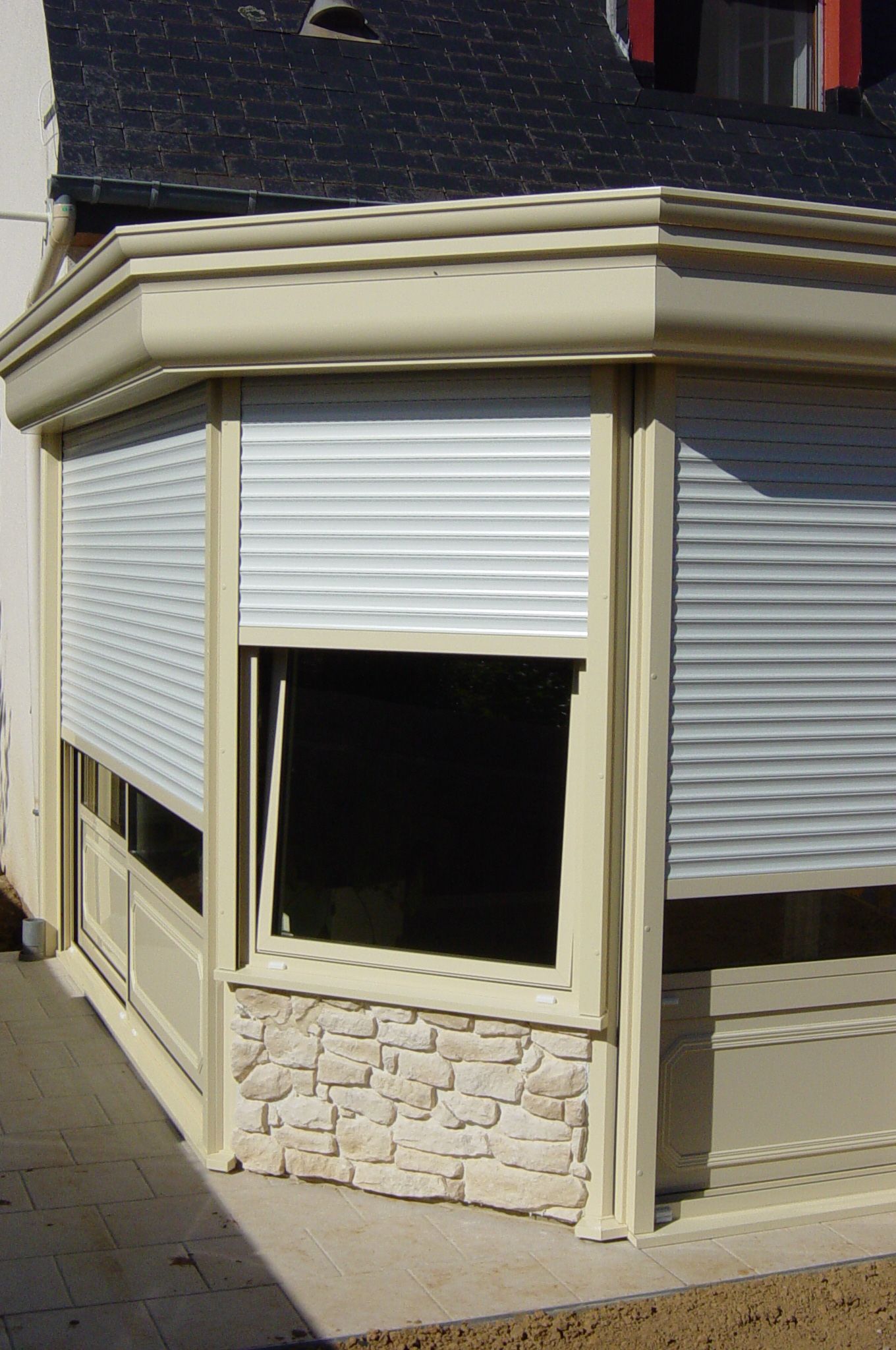Un angle de mur avec une fenêtre et un volet blanc à moitié fermé