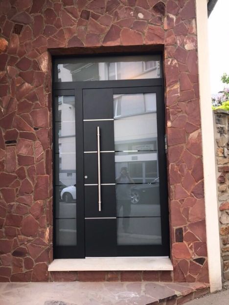 Une porte d'entrée grise en aluminium dans un mur avec une mosaïque de pierres