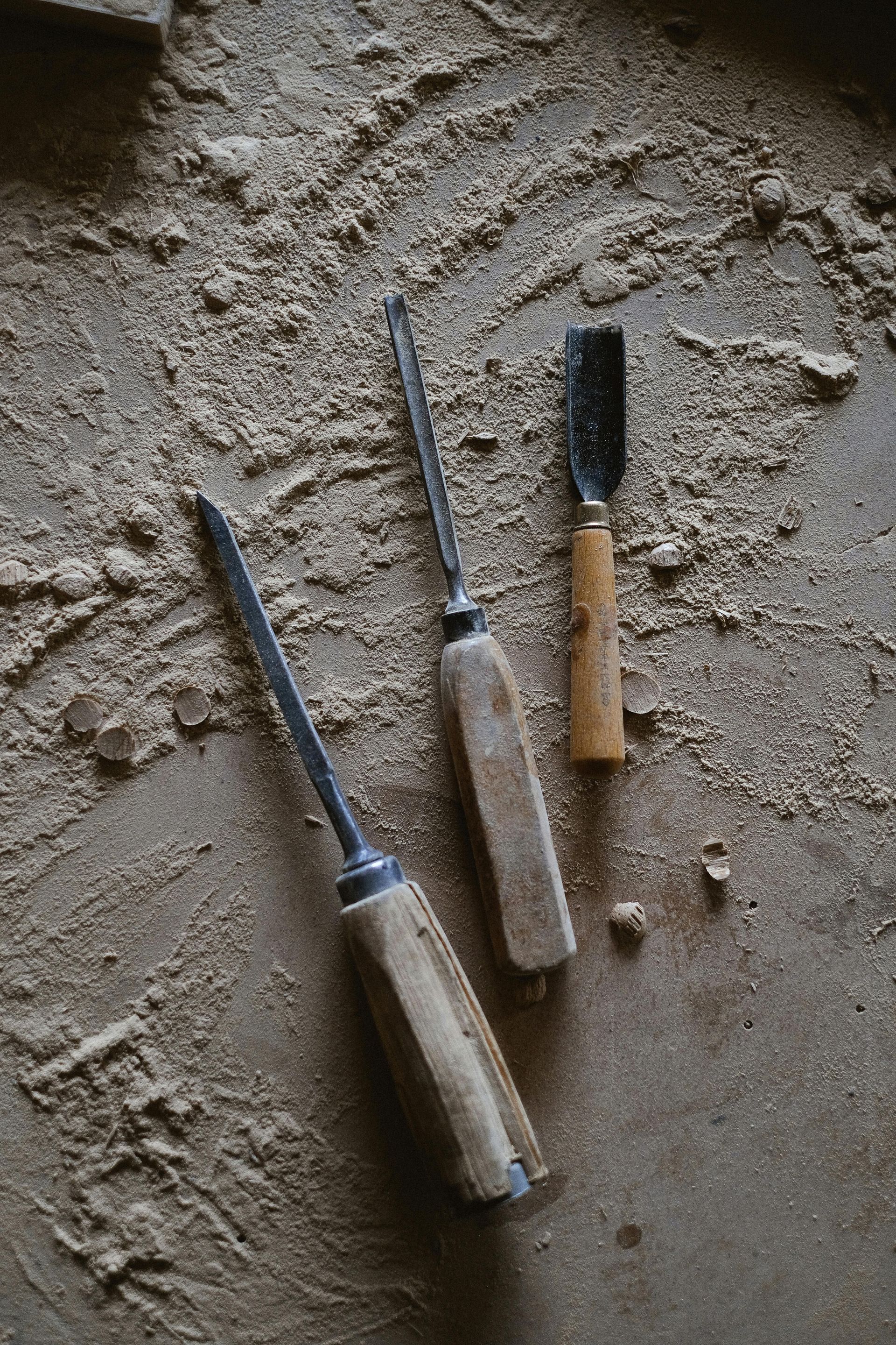 Tres herramientas para tallar madera descansan sobre una superficie polvorienta