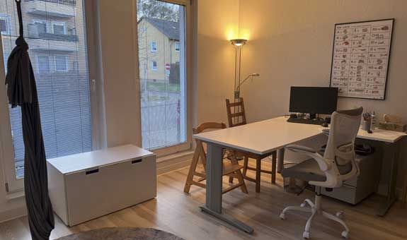 Ein Zimmer mit Schreibtisch, Stuhl und Computer.