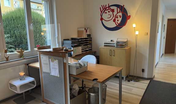 Ein Raum mit einem Tisch, Stühlen, Schränken und einem Smiley an der Wand.