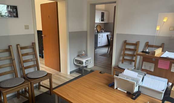 Ein Wartezimmer mit einem Tisch und Stühlen sowie einer Tür, die zu einer Küche führt.