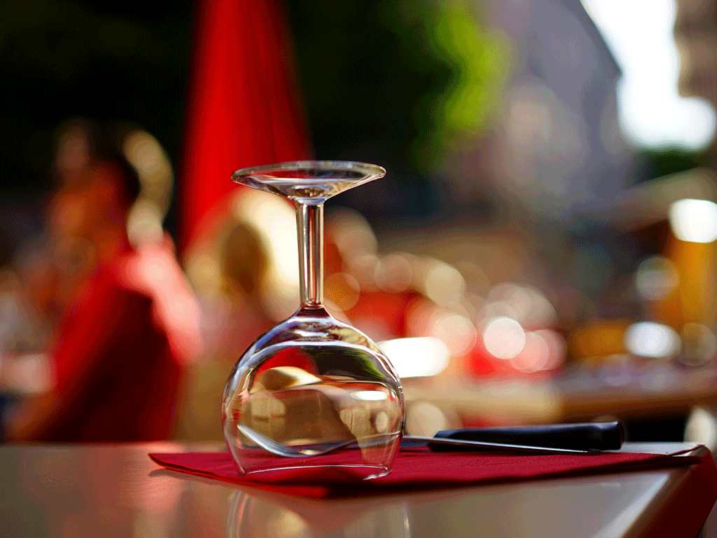 Un verre de vin à l'envers sur une serviette rouge, à la table d'un café en terrasse.