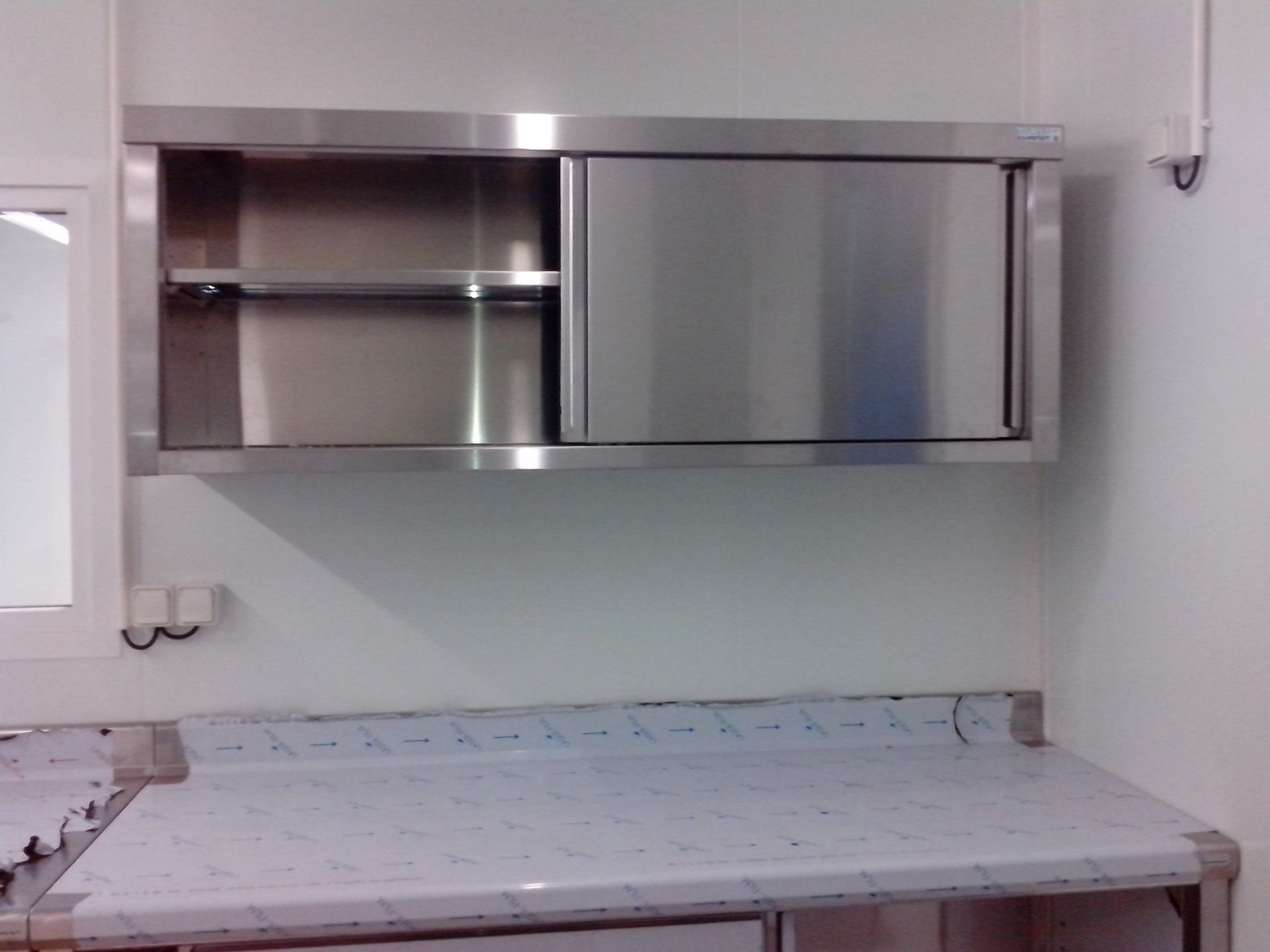 Armoire en acier inoxydable avec porte coulissante au-dessus d'un plan de travail dans une cuisine professionnelle.