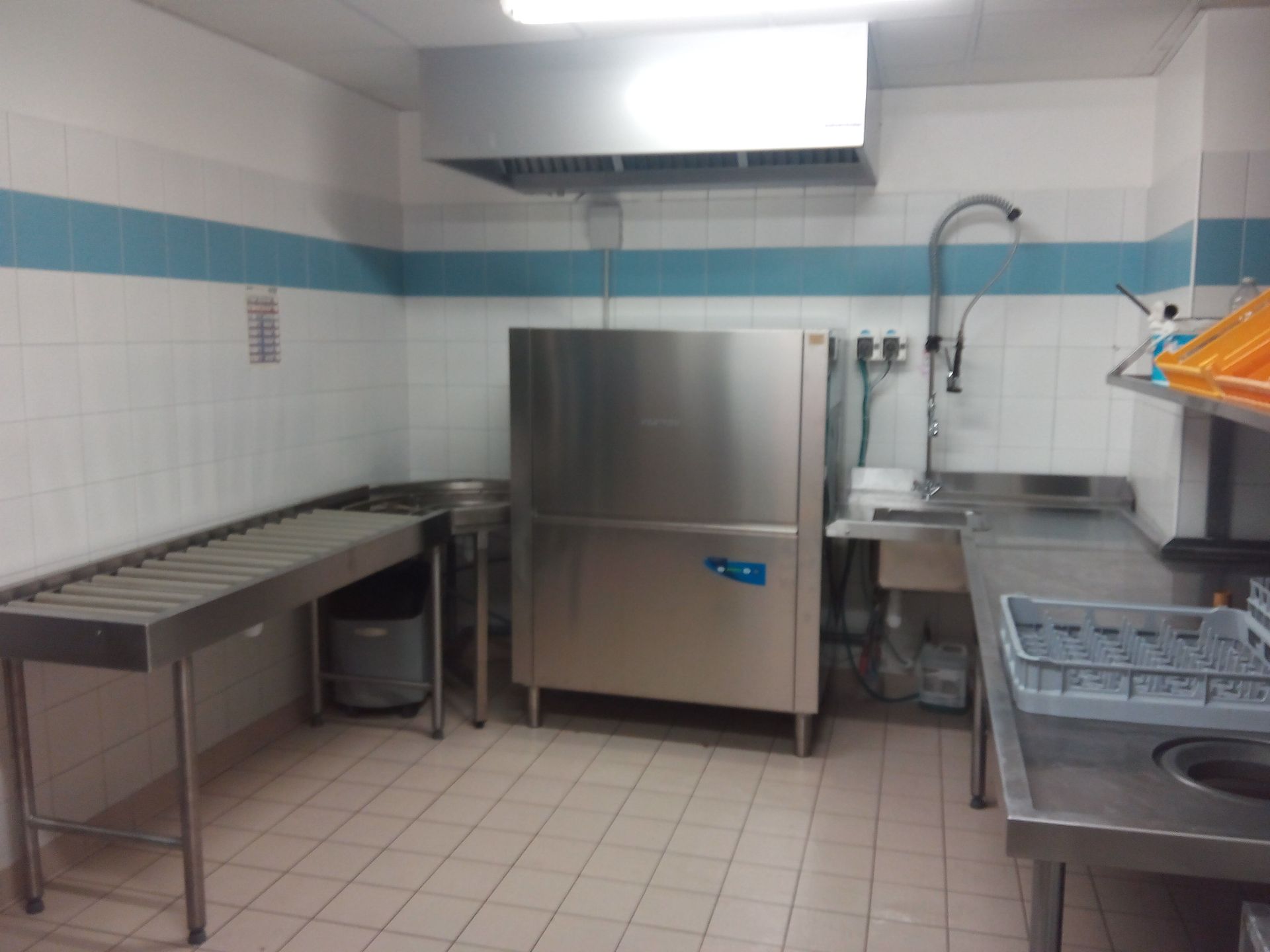 Cuisine professionnelle équipée d'un lave-vaisselle, d'un évier et de plans de travail en acier inoxydable.