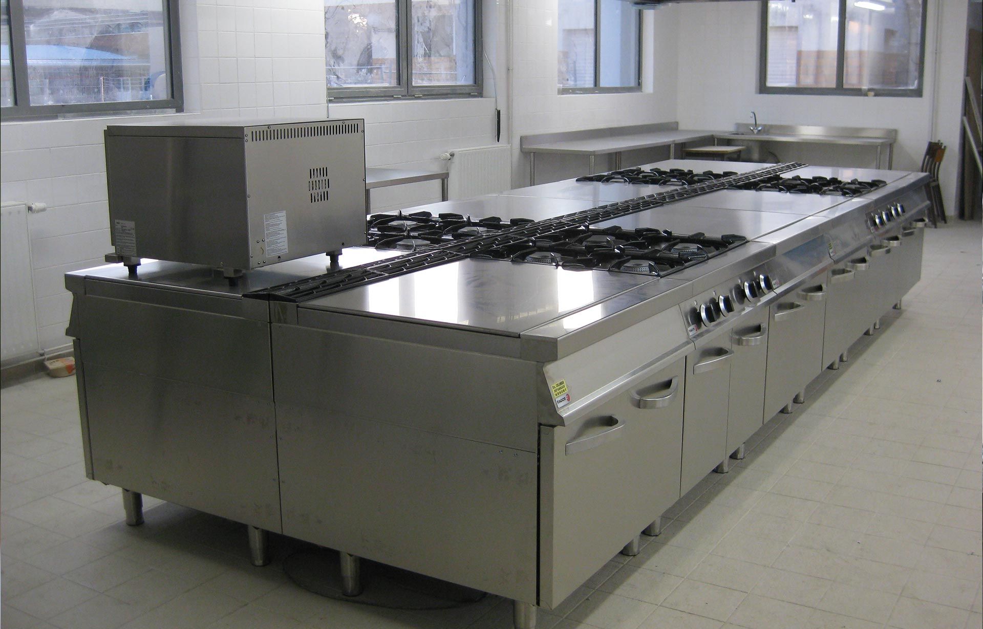 Îlot de cuisine commerciale en acier inoxydable avec plaques de cuisson, brûleurs et armoires.