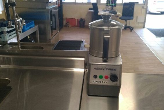 Robot culinaire sur un plan de travail en acier inoxydable dans une cuisine professionnelle.