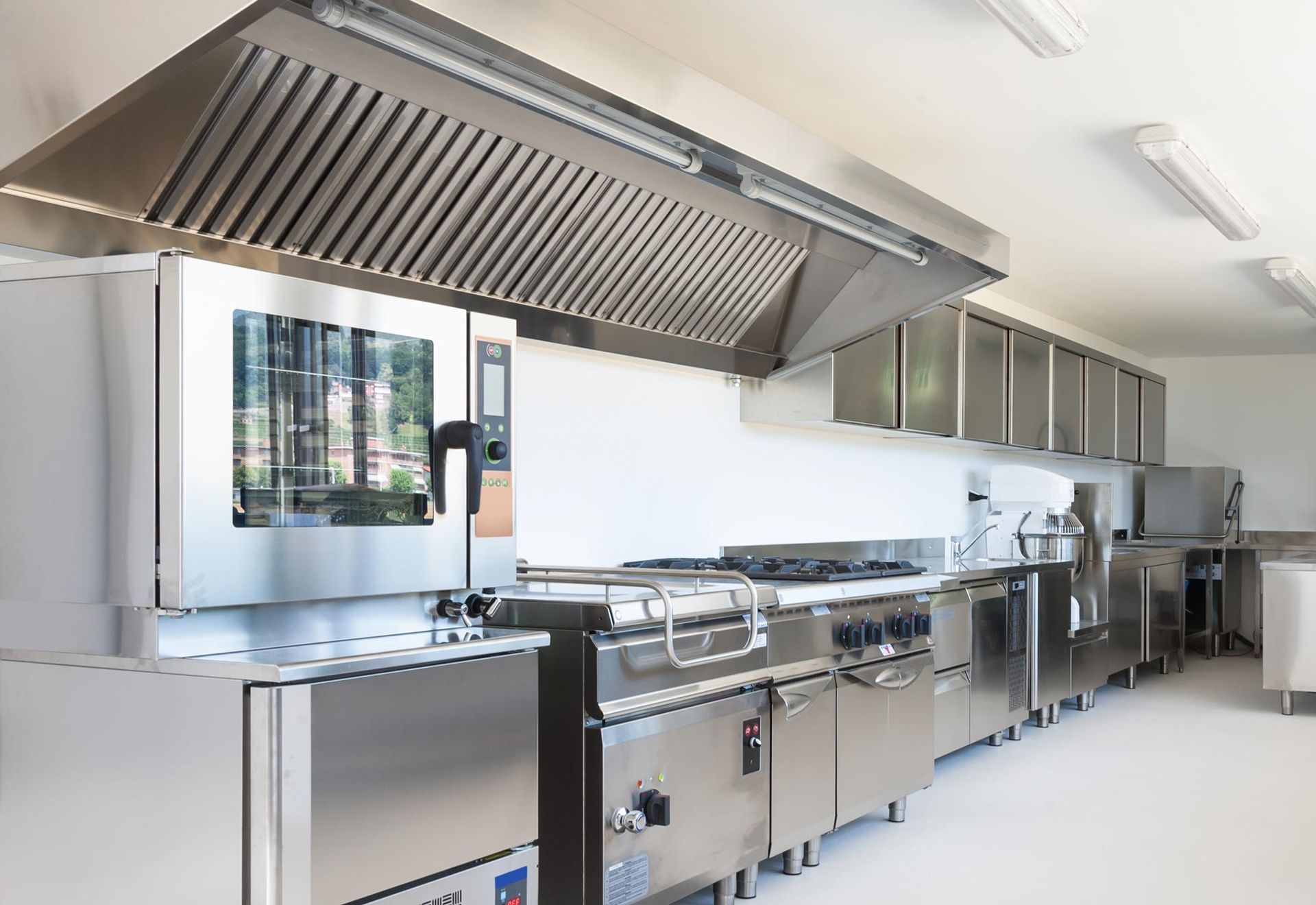 Cuisine commerciale avec appareils électroménagers en acier inoxydable, hotte aspirante et murs blancs.