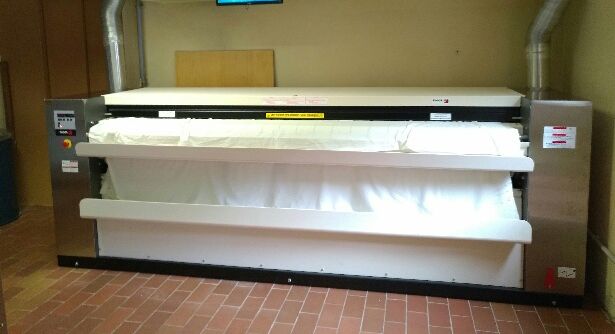 Repasseuse industrielle pour linge plat avec drap blanc dans une pièce.