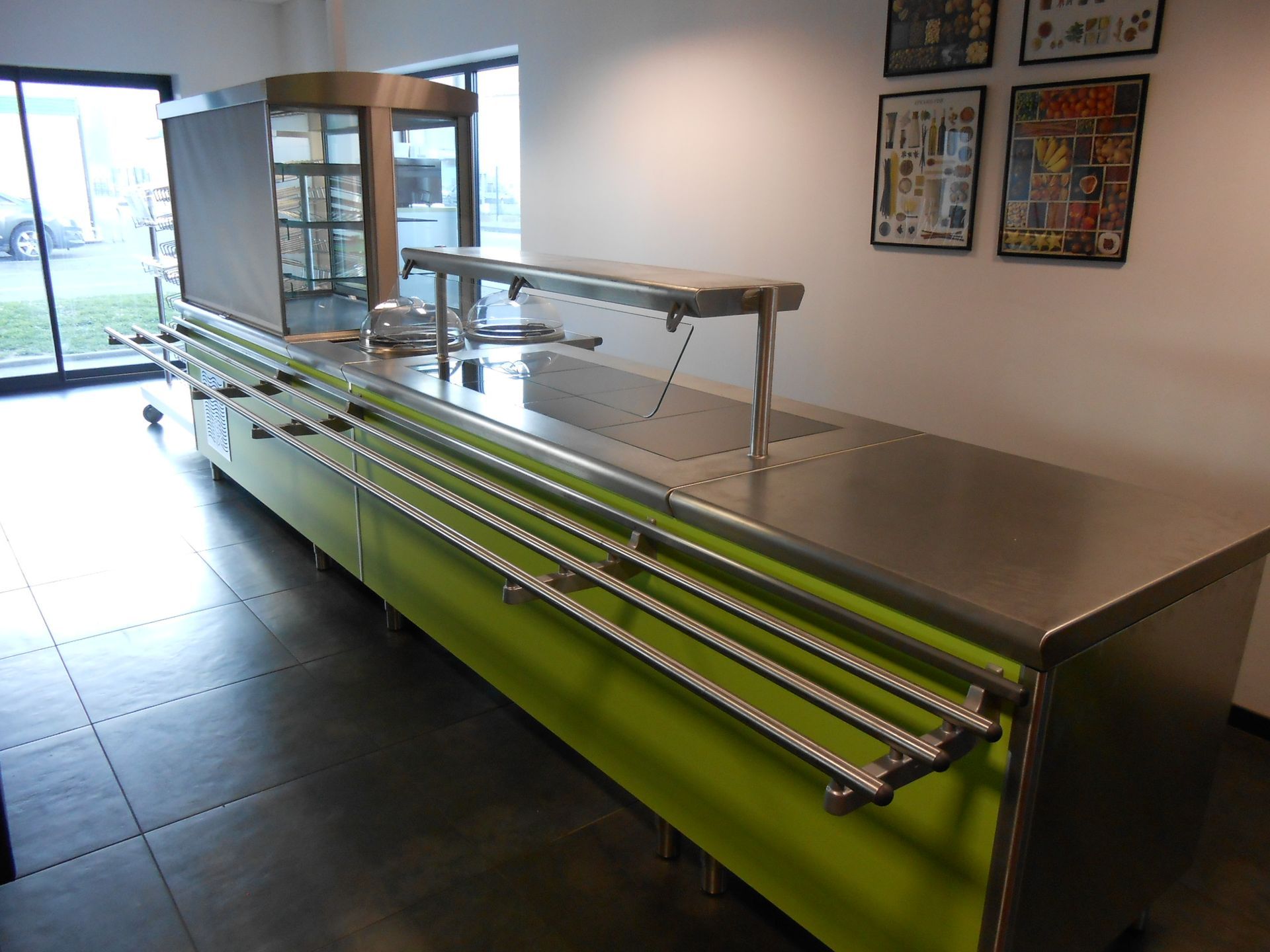 Un buffet commercial en acier inoxydable avec un socle vert vif, dans un intérieur moderne.