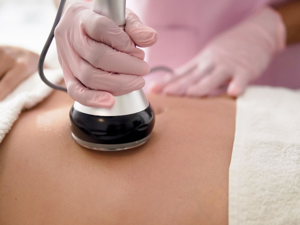 Persona que recibe tratamiento corporal con un dispositivo manual sobre su abdomen, con las manos enguantadas visibles.