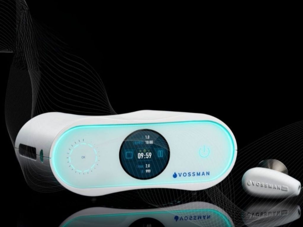 Máquina hidrofacial con pantalla táctil y varios accesorios, color verde azulado y blanco, luces azules brillantes.