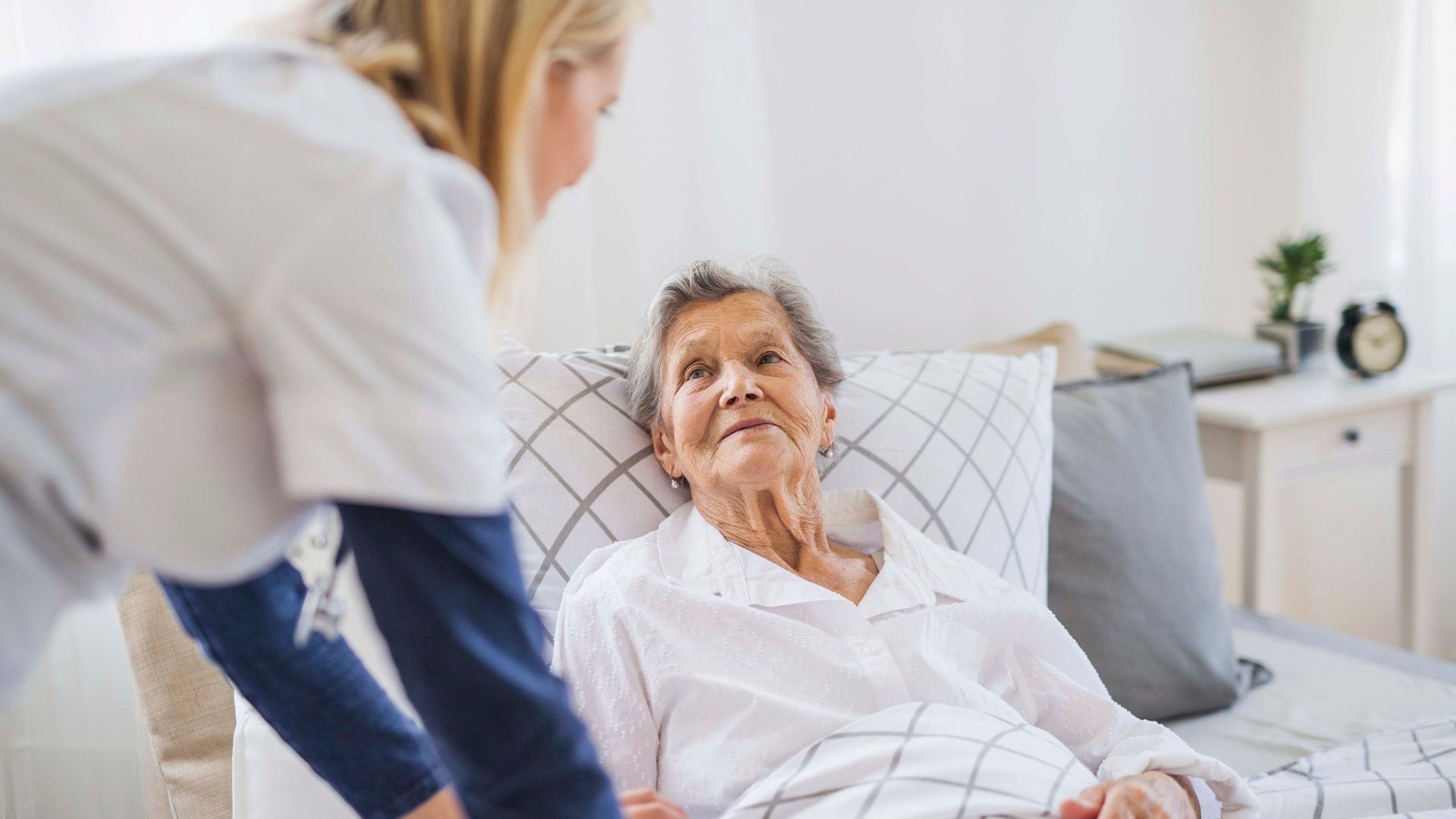 Eine Krankenschwester steht neben einer älteren Frau in einem Krankenhausbett.