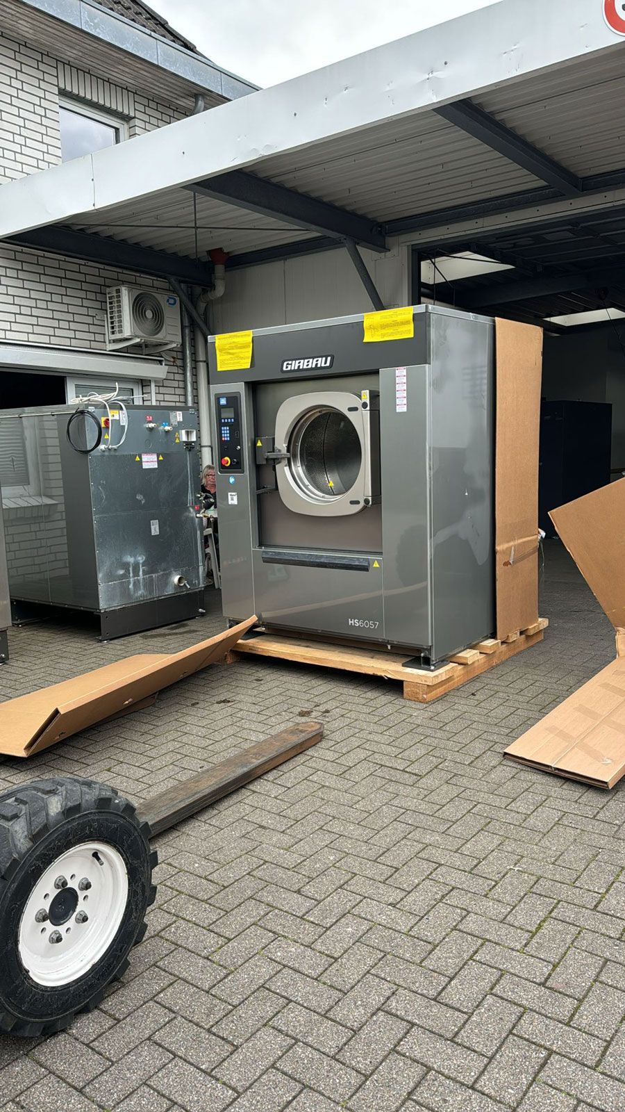 Eine Waschmaschine steht auf einer Holzpalette vor einem Gebäude.