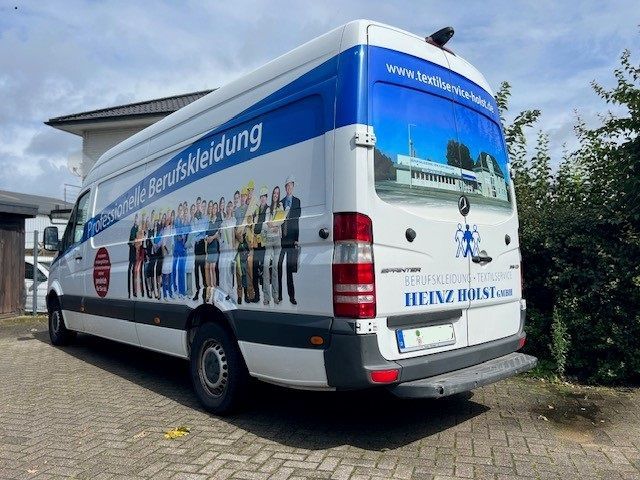 Weißer Lieferwagen mit Firmenlogo, geparkt auf einem gepflasterten Grundstück, Gebäude im Hintergrund.