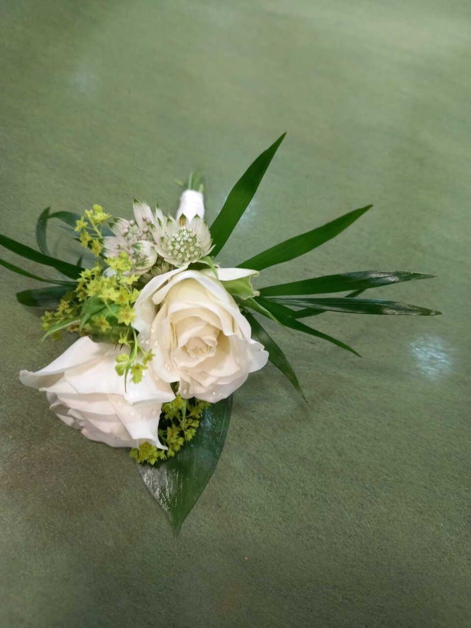 Una rosa blanca con hojas verdes está sobre una mesa.