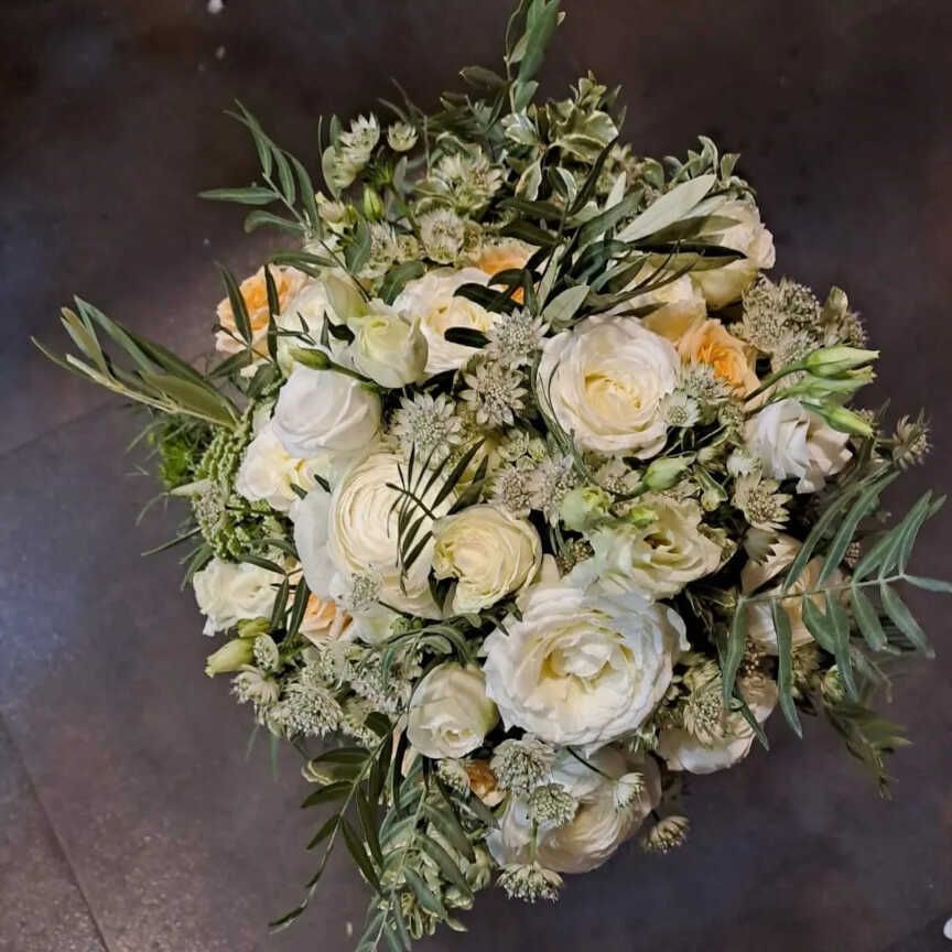 Un ramo de flores blancas y vegetación está sobre una mesa.