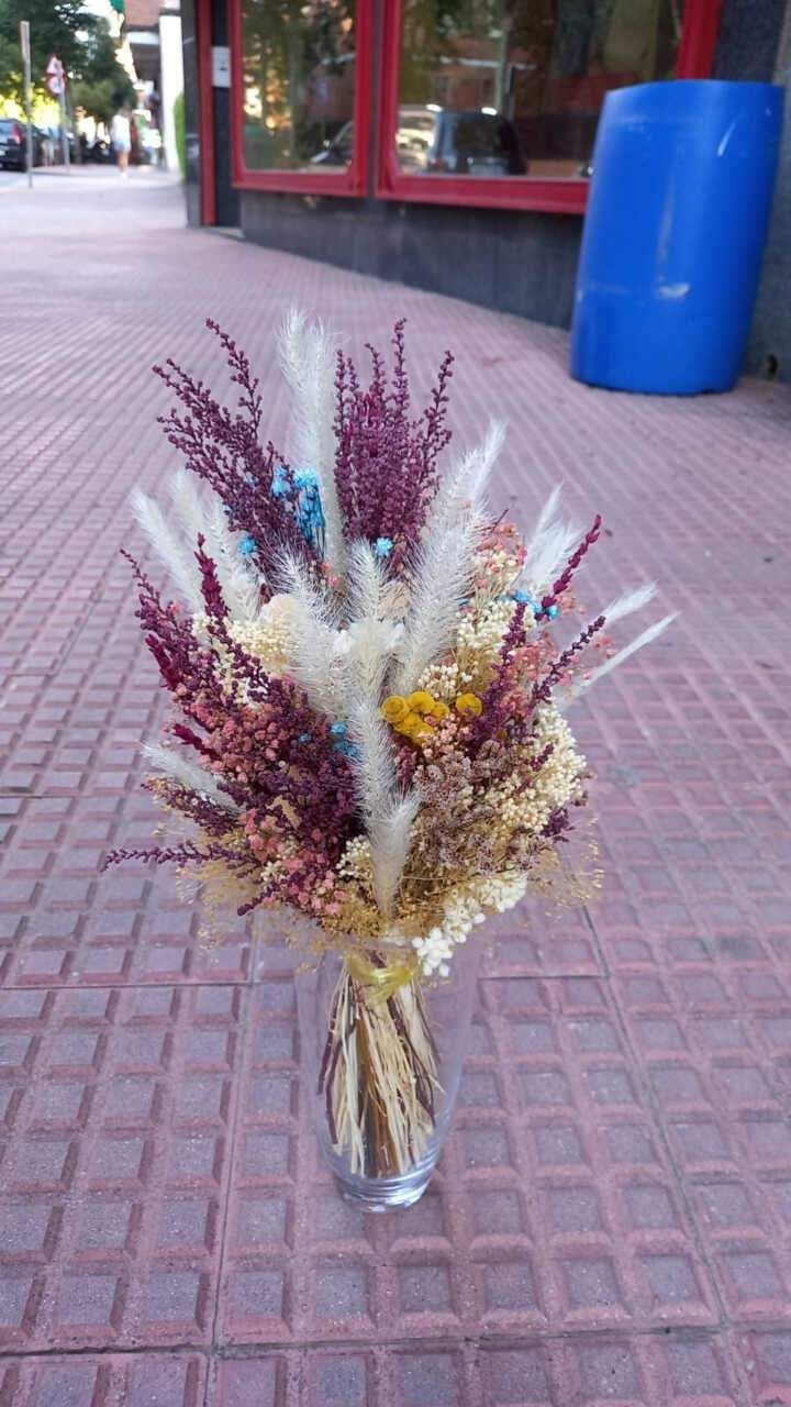 Un jarrón lleno de flores secas está sobre una acera.