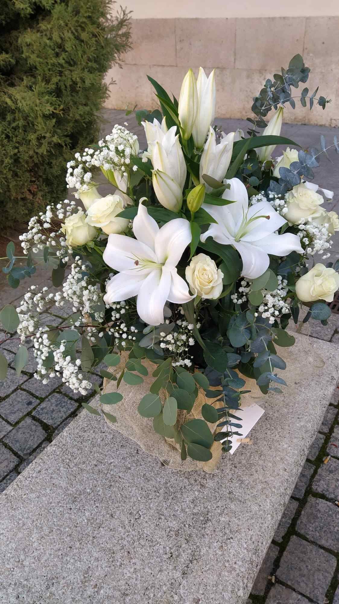 Un jarrón lleno de flores blancas reposa sobre un banco de piedra.