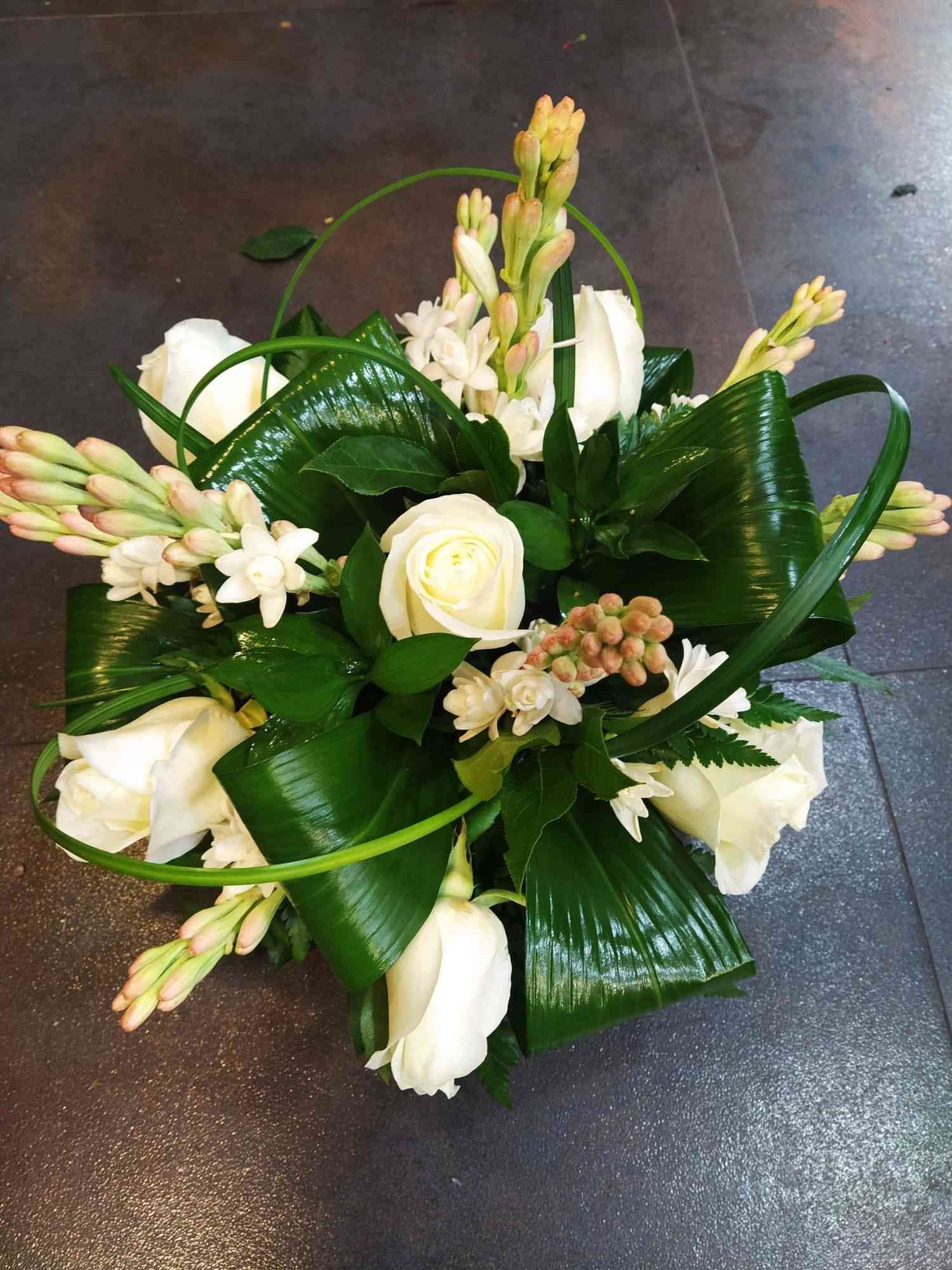 Un ramo de flores blancas y vegetación sobre una mesa.