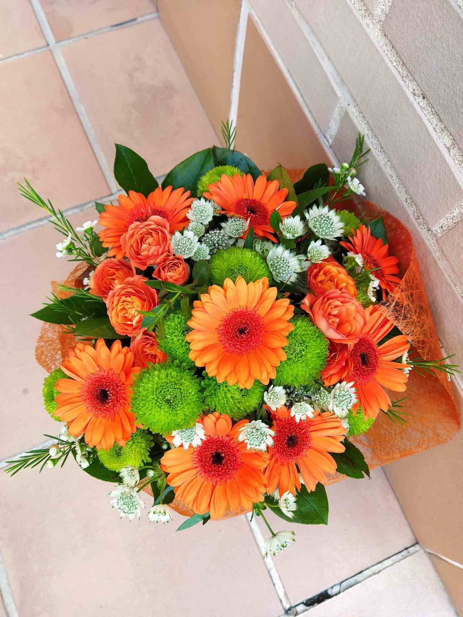 Un ramo de flores naranjas y verdes está sobre un suelo de baldosas.