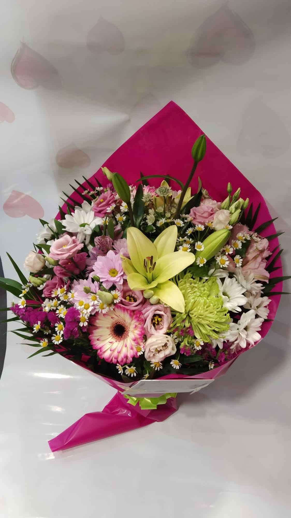 Un ramo de flores envuelto en papel rosa está sobre una mesa.